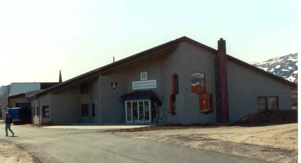 A grey building with a steep roof and red details