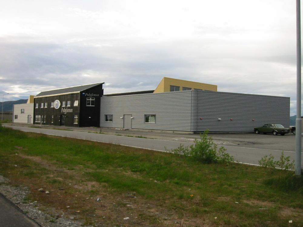 A dark building beside a long hall with striped grey cladding