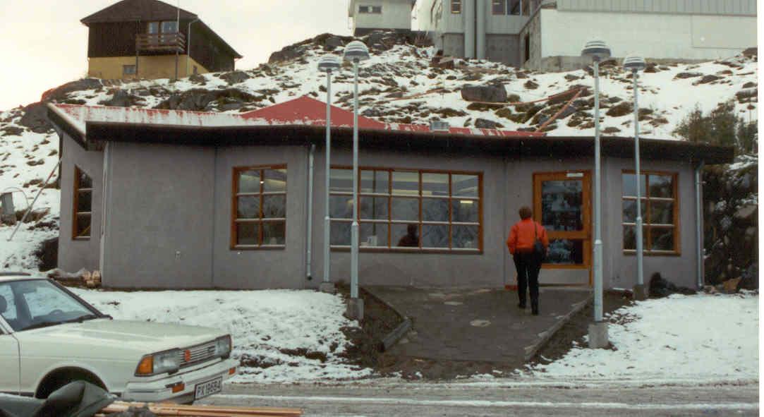 A grey building with large windows and snow on the ground
